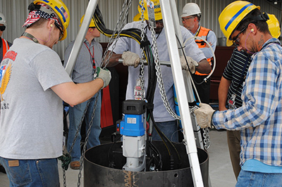 Workers test a modified cutting tool in a mock demonstration before using it to modify storage positions for waste canisters inside the Glass Waste Storage Building 1